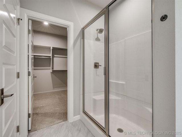 full bathroom featuring a walk in closet, marble finish floor, baseboards, and a stall shower