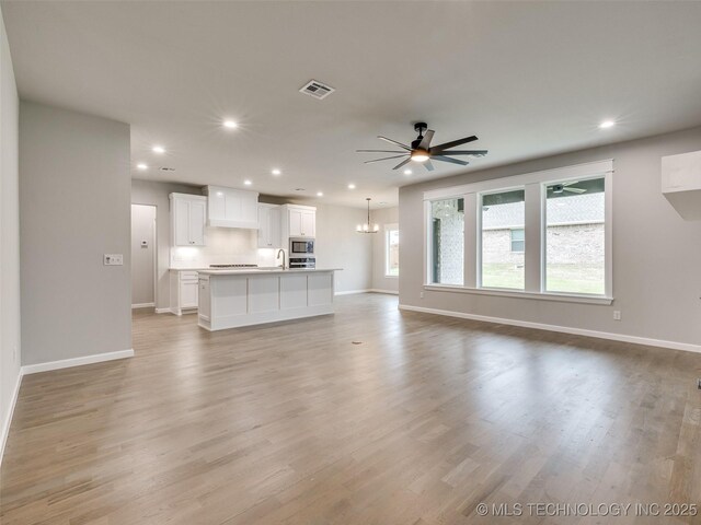 unfurnished living room featuring baseboards, visible vents, recessed lighting, light wood-style floors, and ceiling fan with notable chandelier