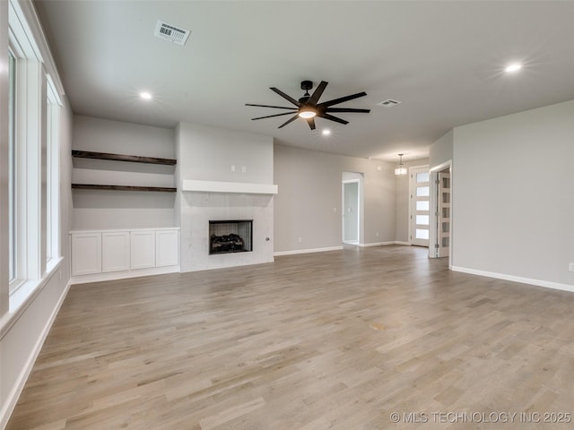 unfurnished living room featuring light wood-type flooring, a ceiling fan, visible vents, and a fireplace