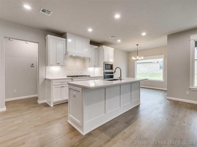 kitchen featuring white cabinets, stainless steel appliances, visible vents, baseboards, and a kitchen island with sink