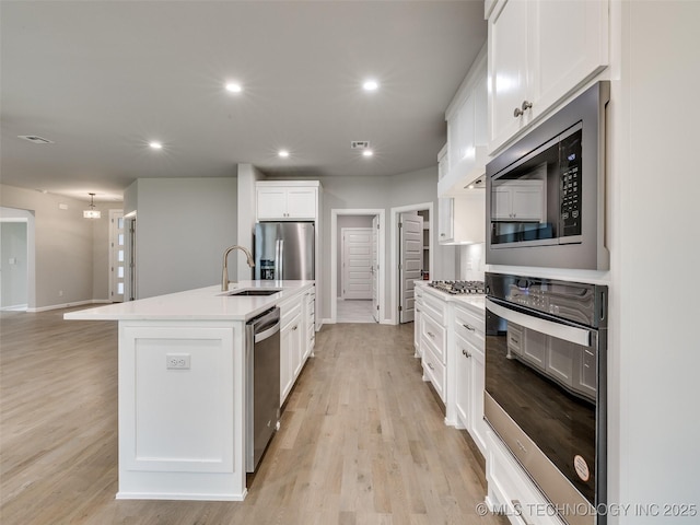 kitchen with light wood-style flooring, white cabinetry, stainless steel appliances, and a sink