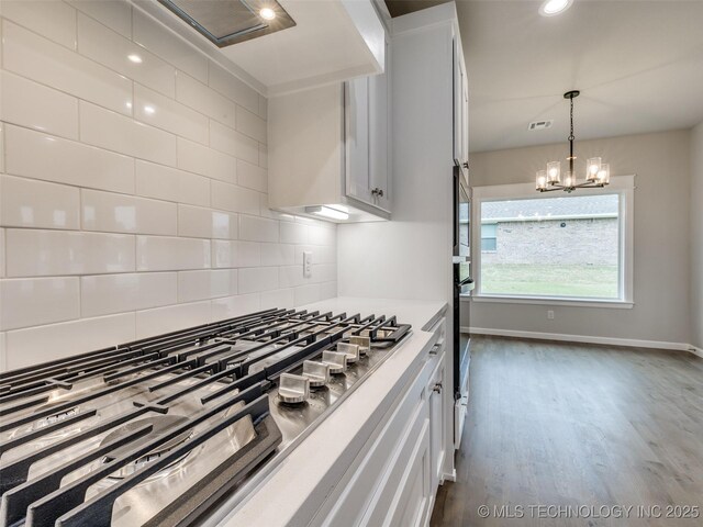 kitchen featuring dark wood finished floors, a notable chandelier, stainless steel gas stovetop, decorative backsplash, and light countertops