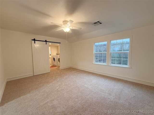 unfurnished bedroom featuring ceiling fan, independent washer and dryer, a barn door, and carpet flooring