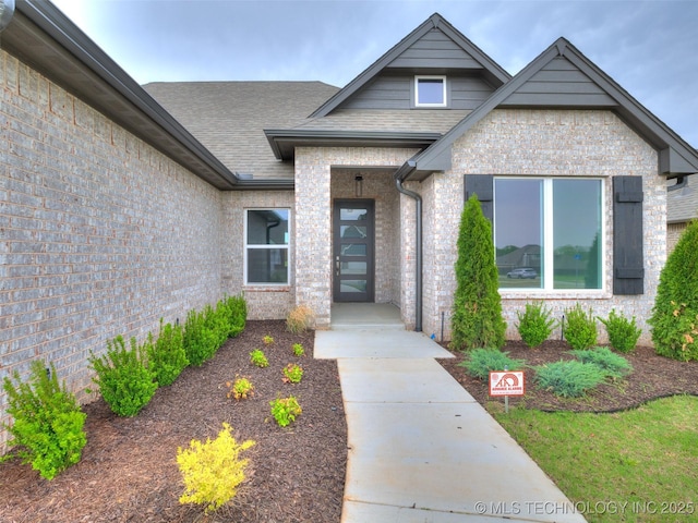 doorway to property featuring brick siding and roof with shingles