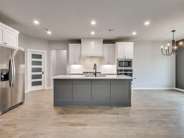 kitchen featuring a notable chandelier, stainless steel appliances, white cabinetry, and premium range hood