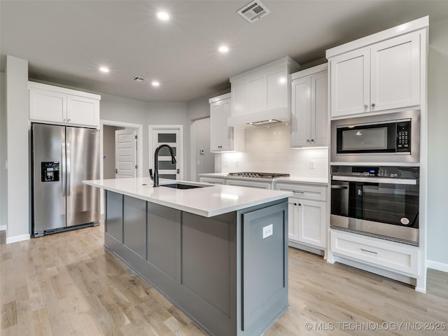 kitchen with stainless steel appliances, visible vents, a sink, a kitchen island with sink, and tasteful backsplash