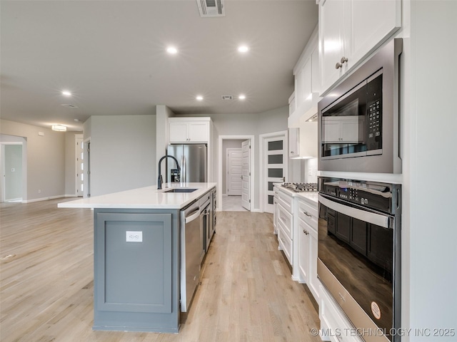 kitchen featuring visible vents, a sink, light wood-style flooring, appliances with stainless steel finishes, and white cabinetry
