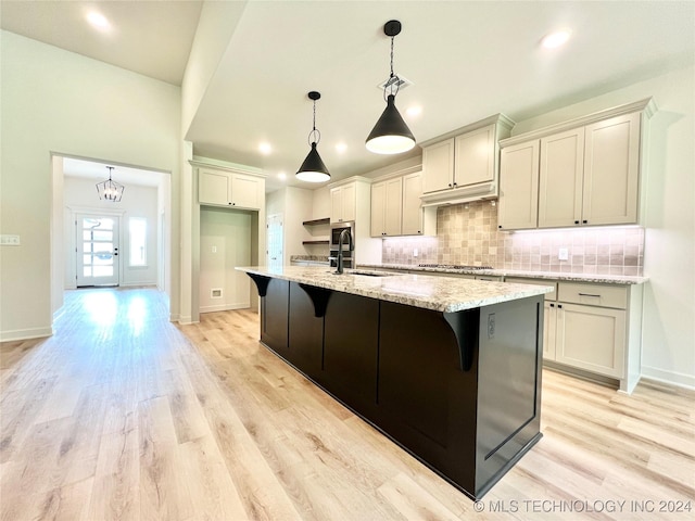 kitchen featuring light stone counters, hanging light fixtures, a kitchen island with sink, a sink, and a kitchen bar