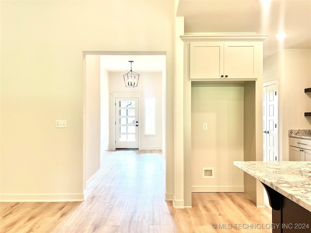 kitchen featuring light stone counters, pendant lighting, a notable chandelier, light wood-style floors, and baseboards