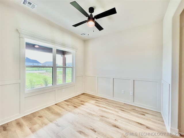 spare room featuring light wood-type flooring, visible vents, ceiling fan, and a decorative wall