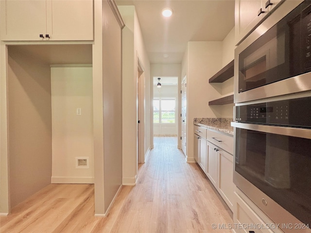 kitchen featuring light wood finished floors, open shelves, appliances with stainless steel finishes, white cabinetry, and light stone countertops