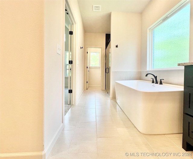 bathroom with a freestanding tub, tile patterned flooring, visible vents, and baseboards