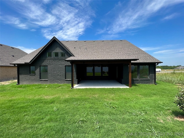 back of house with brick siding, a shingled roof, a yard, and a patio