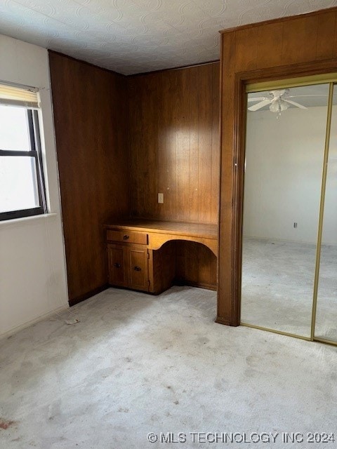 interior space featuring a textured ceiling, built in desk, ceiling fan, and wooden walls