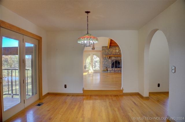 unfurnished dining area featuring a notable chandelier, plenty of natural light, a stone fireplace, and light wood-type flooring