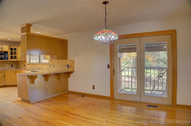 kitchen featuring sink, hanging light fixtures, kitchen peninsula, a breakfast bar, and light wood-type flooring