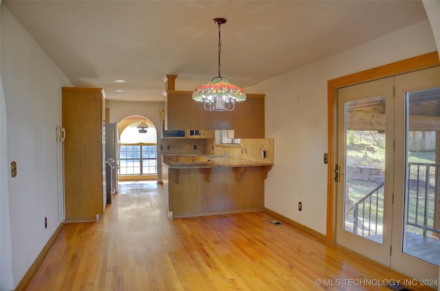 kitchen featuring kitchen peninsula, a kitchen breakfast bar, tasteful backsplash, light hardwood / wood-style flooring, and hanging light fixtures