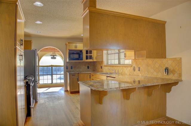 kitchen featuring sink, kitchen peninsula, a kitchen bar, decorative backsplash, and light wood-type flooring