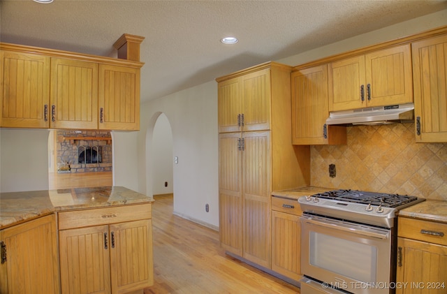 kitchen with light stone countertops, light wood-type flooring, tasteful backsplash, a fireplace, and stainless steel gas stove