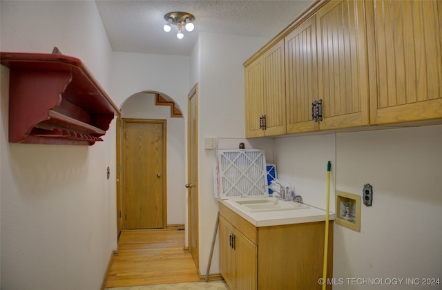 laundry room with cabinets, sink, hookup for a washing machine, a textured ceiling, and light hardwood / wood-style floors