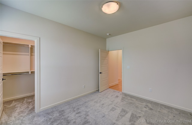 unfurnished bedroom with light carpet, a spacious closet, and a closet