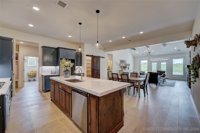 kitchen featuring a center island with sink, sink, a barn door, appliances with stainless steel finishes, and decorative light fixtures