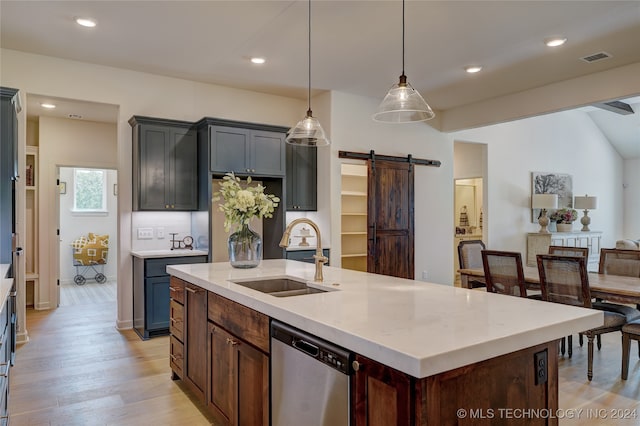 kitchen with sink, a barn door, stainless steel dishwasher, decorative light fixtures, and a kitchen island with sink