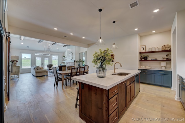 kitchen with sink, stainless steel dishwasher, decorative light fixtures, a center island with sink, and light wood-type flooring