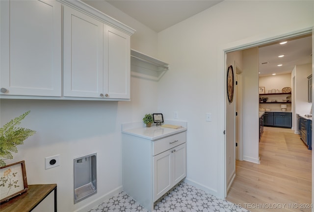 washroom with electric dryer hookup, cabinets, and light wood-type flooring