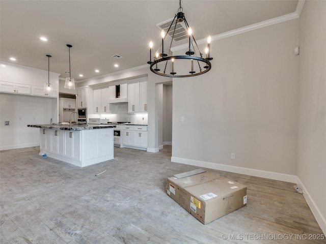 kitchen with wall chimney exhaust hood, white cabinets, hanging light fixtures, and a kitchen island with sink