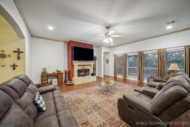 living room featuring a tile fireplace, ceiling fan, crown molding, and wood-type flooring