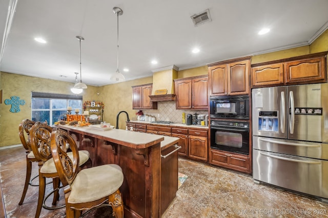 kitchen with premium range hood, black appliances, a center island with sink, crown molding, and decorative light fixtures