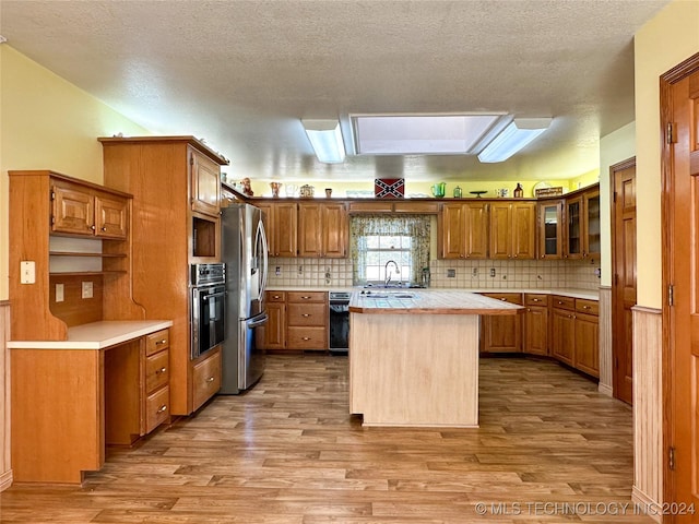 kitchen featuring a kitchen island, a skylight, stainless steel fridge with ice dispenser, oven, and light wood-type flooring