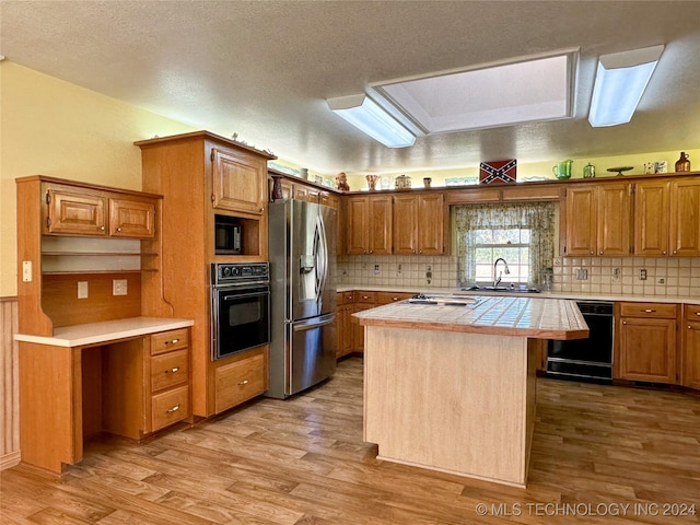 kitchen featuring black appliances, tile counters, a kitchen island, sink, and light wood-type flooring