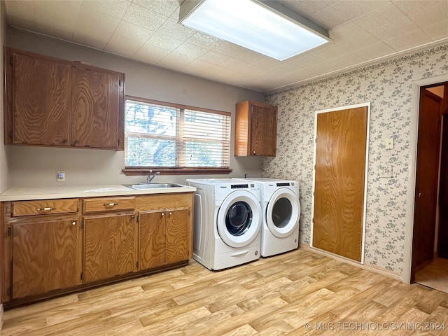 clothes washing area featuring light hardwood / wood-style flooring, independent washer and dryer, sink, and cabinets