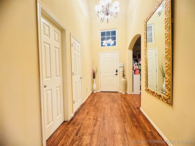 doorway to outside with wood-type flooring, an inviting chandelier, and a high ceiling