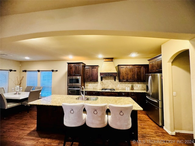 kitchen featuring sink, an island with sink, dark hardwood / wood-style flooring, custom range hood, and stainless steel appliances