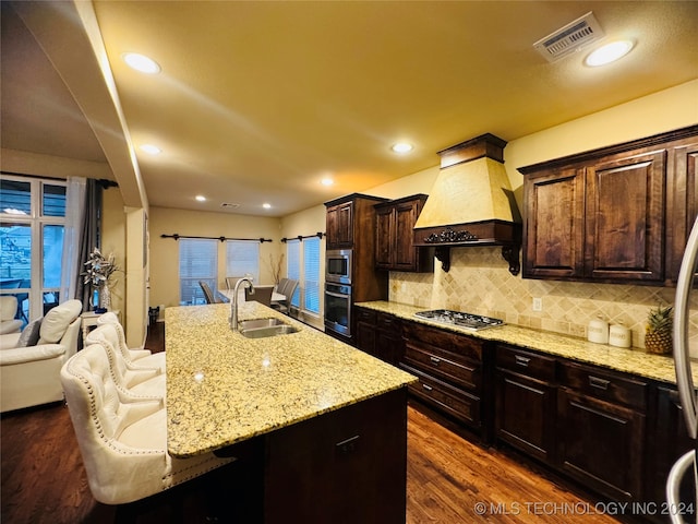 kitchen with custom exhaust hood, a breakfast bar, stainless steel appliances, sink, and an island with sink