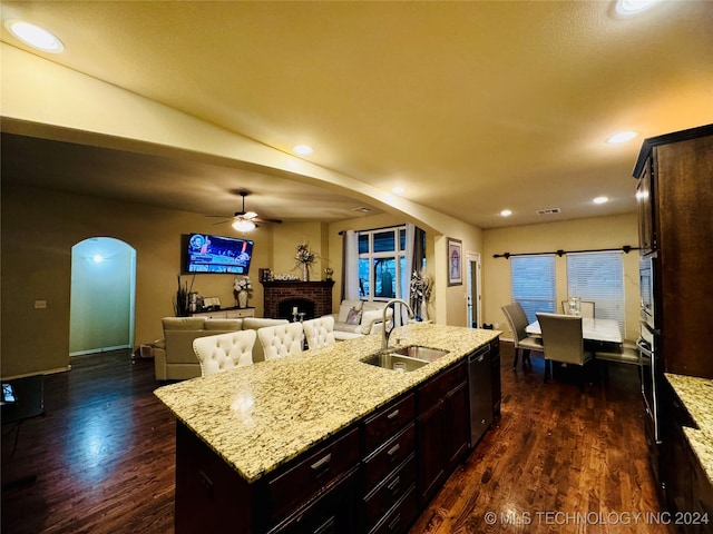 kitchen with sink, a brick fireplace, light stone counters, dark hardwood / wood-style floors, and a center island with sink