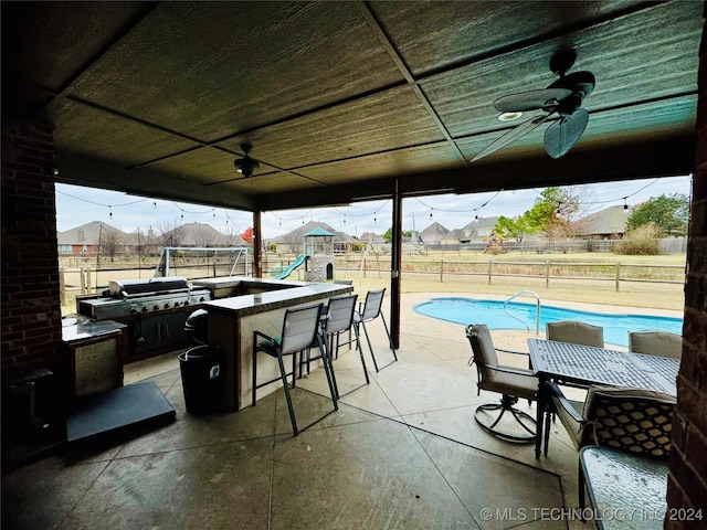 view of patio featuring a fenced in pool, grilling area, an outdoor bar, ceiling fan, and exterior kitchen