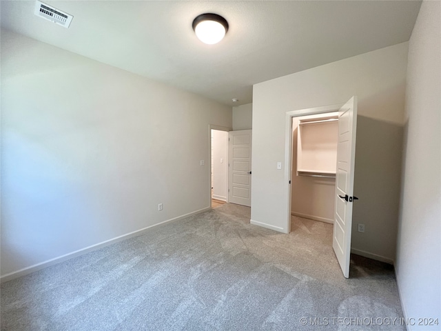 unfurnished bedroom with a walk in closet, light carpet, and a closet