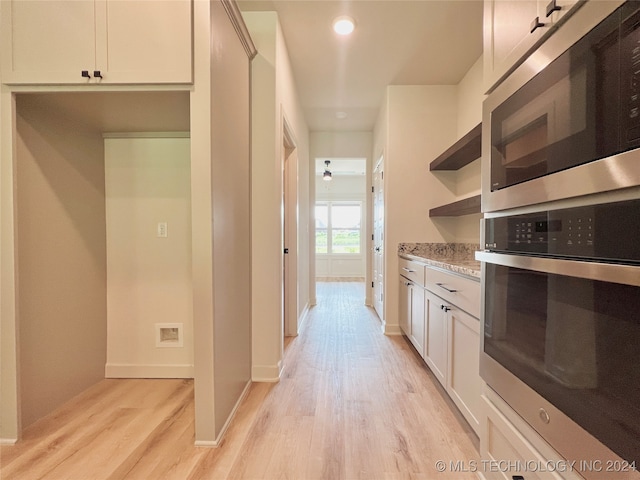 kitchen featuring stainless steel appliances, light stone countertops, white cabinets, and light wood-type flooring