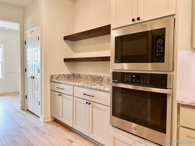 kitchen with stainless steel appliances, white cabinetry, light stone countertops, and light wood-type flooring