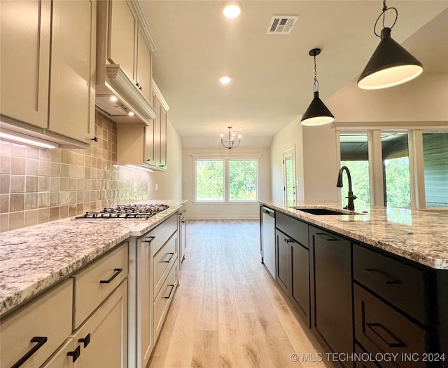 kitchen with sink, light stone counters, hanging light fixtures, appliances with stainless steel finishes, and light hardwood / wood-style floors