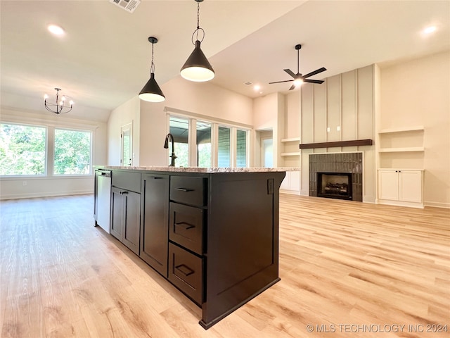 kitchen featuring built in features, decorative light fixtures, dishwasher, a tiled fireplace, and a kitchen island with sink