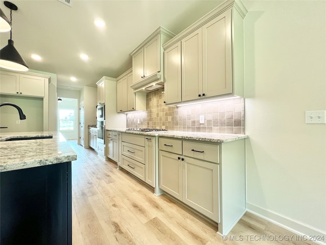 kitchen with pendant lighting, sink, decorative backsplash, light stone counters, and light hardwood / wood-style flooring