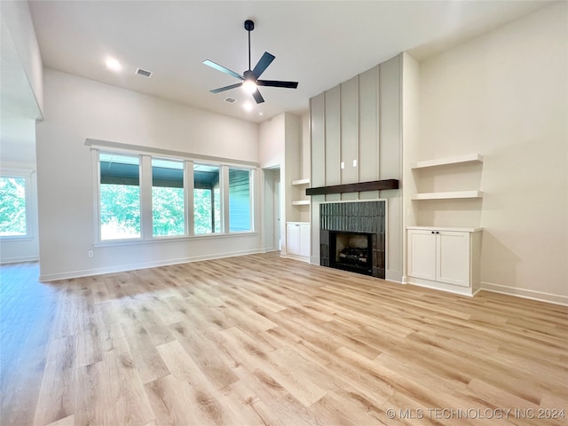 unfurnished living room with a tiled fireplace, built in features, light hardwood / wood-style floors, and ceiling fan