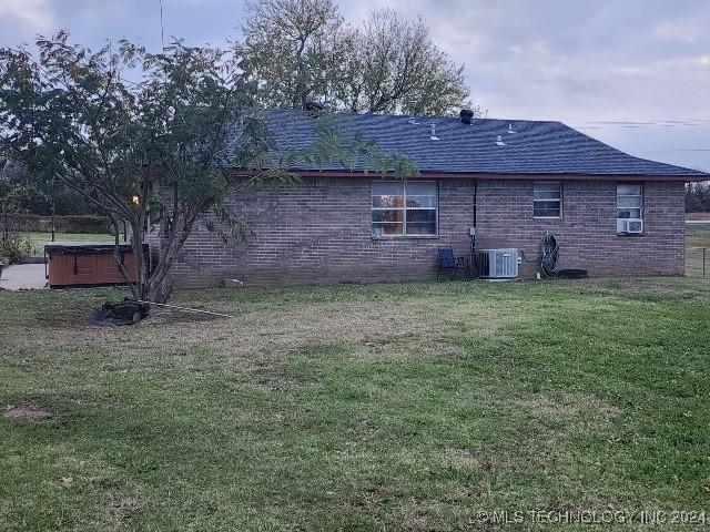 rear view of house featuring a hot tub, cooling unit, and a lawn