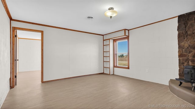 empty room with a wood stove, ornamental molding, and light hardwood / wood-style flooring