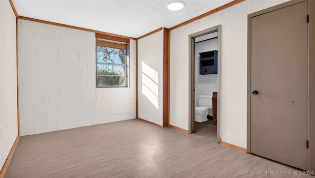 unfurnished bedroom featuring a textured ceiling, ensuite bathroom, light hardwood / wood-style flooring, and ornamental molding